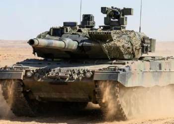 A front-view of the German Leopard 2A7+ Main Battle Tank (MBT) maneuvering in desert terrain. The image highlights the Rheinmetall 120mm L55A1 smoothbore gun, modular add-on armor for urban protection, and the FLW 200 remote weapon station on the turret.