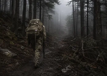 Exhausted soldier carrying a heavy ruck walks alone into a dark foggy forest after failing Special Forces Assessment and Selection (SFAS)